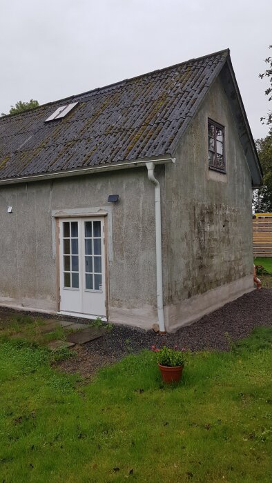 Ett slitet hus med mossa på taket, fransk balkongdörr, kruka med blommor, smutsiga väggar.