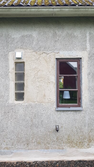 Vägg med fönster, yttre eluttag, samt ventilationsgaller på en byggnad med takmossa.