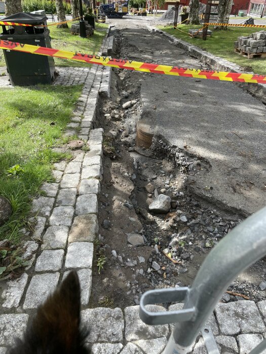 Gatuarbete, avspärrat område, grävmaskin, uppgrävd asfalt, stenkantsten, grön gräs, säkerhetstejp.