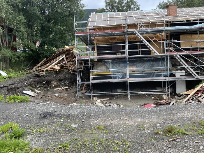 Hus under renovering eller ombyggnad med byggställningar, spillror och en hög med rivningsavfall.