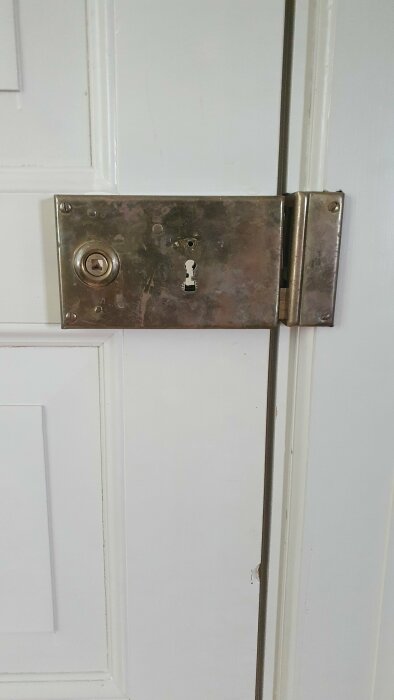 En vit dörr med en metall låsbleckplatta, nyckelhål och säkerhetslåsets vridknapp.