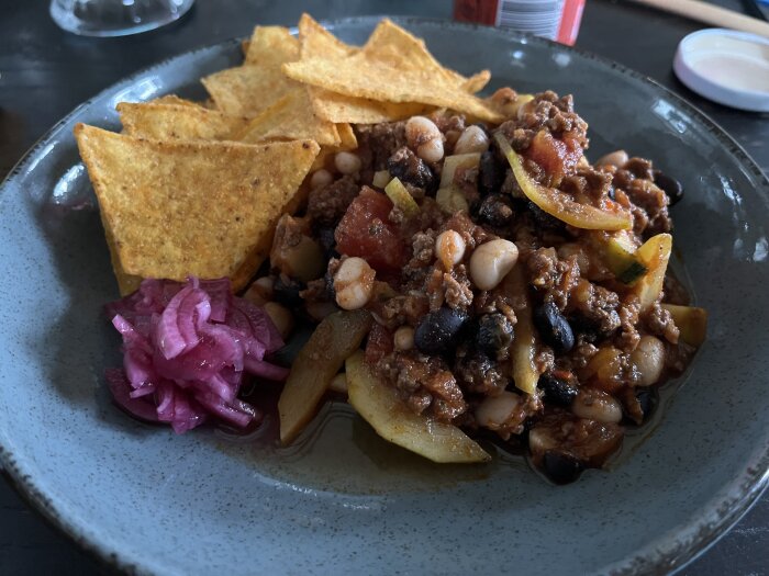 Chili med bönor och köttfärs, tortillachips, inlagd rödlök, i en skål.