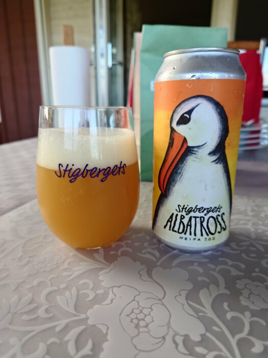 En ölburk med albatross-motiv bredvid ett ölglas på ett mönstrat bord.