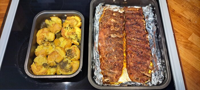 Grillade revbensspjäll och krossade kryddiga potatisar i ugnsformar på spishäll. Delicious looking ribs and smashed seasoned potatoes in oven trays.