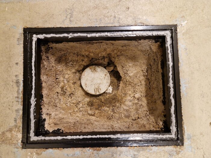 Golvinspektionslucka öppen, vit tätningsmassa, sand, röränd, byggarbetsplats eller renovering pågår.