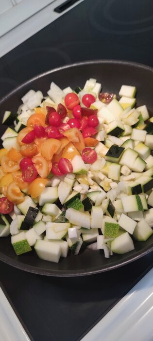 Stekpanna med tärnad zucchini, hackad lök och halverade körsbärstomater, förberedelse för matlagning.