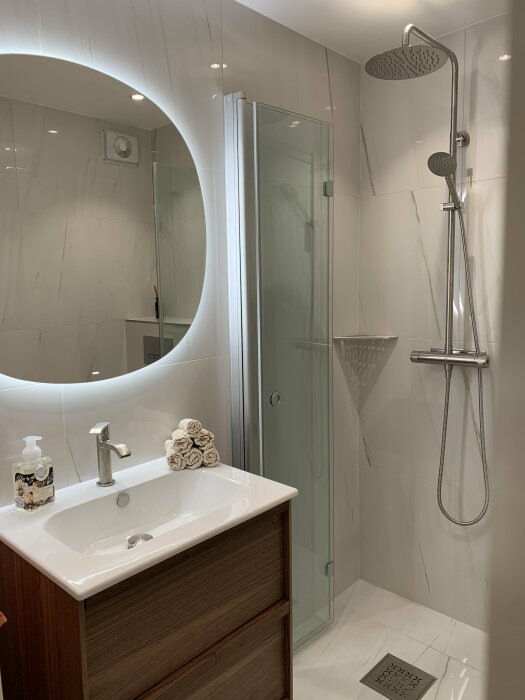 Modernt badrum, vit och grå inredning, duschkabin, tvättställ, spegel, handdukar.