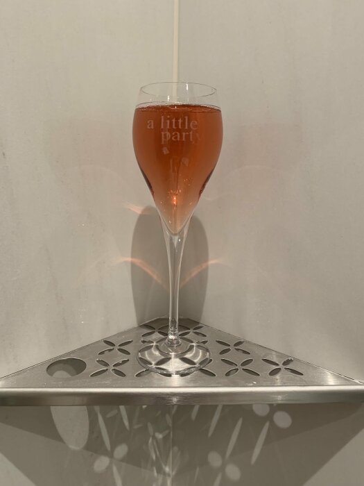 Ett champagneflöjt med rosa dryck och texten "a little party" står på ett dekorativt fat.