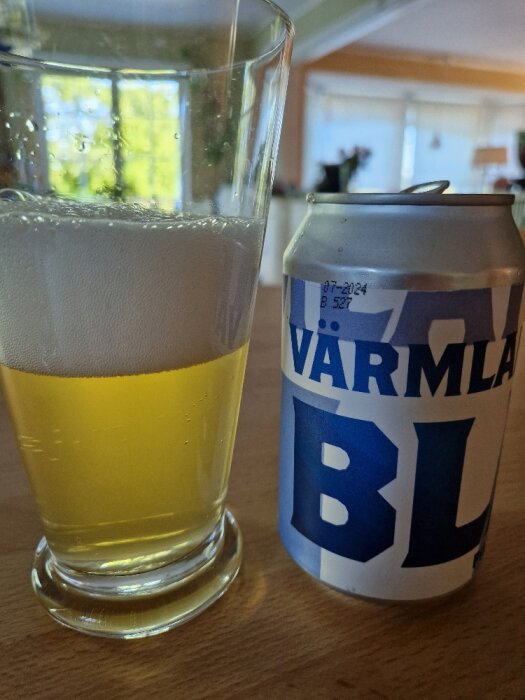 Glas med ljus dryck och skum, burk märkt "VÄRMLANDS", inomhusmiljö, suddig bakgrund, kök eller vardagsrum.