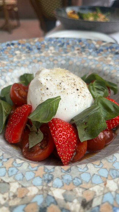 Mozzarella, jordgubbar, basilika, körsbärstomater, peppar på tallrik. Fräsch färgglad sallad, gastronomisk presentation, måltid utomhus.