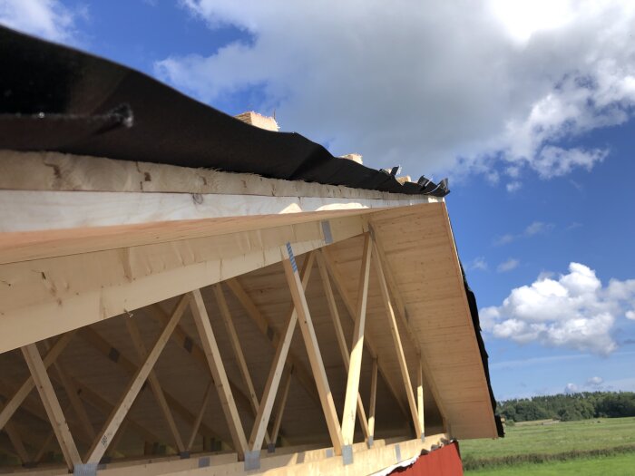 Byggnadsställning och takkonstruktion under uppbyggnad, med blå himmel och moln i bakgrunden.