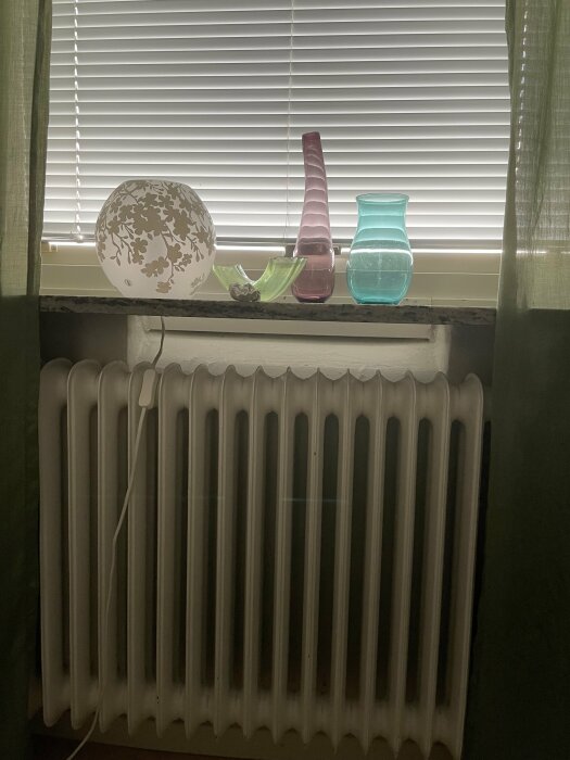 Fönster med persienner, olika glasföremål på fönsterbräda, lampa, radiator, diskret belysning, inomhus, gardiner.