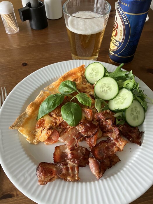 Pizza med bacon, sallad och gurka, öl i glas, alkoholfri ölburk, kryddor, träbord.