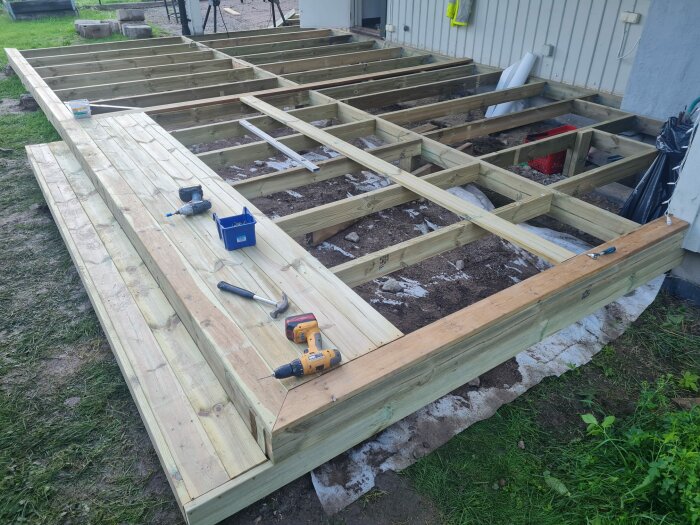 Påbörjad trätrallkonstruktion, verktyg, oavslutat byggprojekt utomhus vid husvägg.