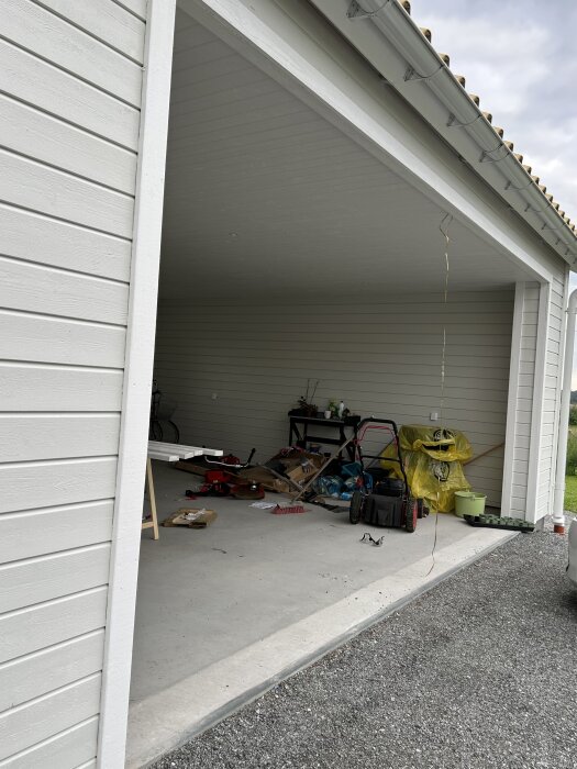 Ett öppet garage fyllt med diverse föremål, verktyg, och röra, dagtid.