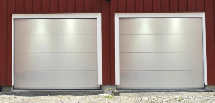 Två garageportar i metall, röd vägg, marken framför, liten grön växt.