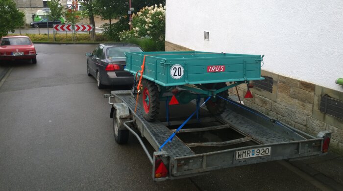 Grön släpvagn märkt "IRUS" lastad på grå trailer, på parkeringsplats, hastighetsskylt "20" fäst vid släpvagn.