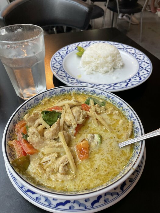 Restaurangbord med thailändsk gröncurry med kyckling, ett fat ris och ett glas vatten.