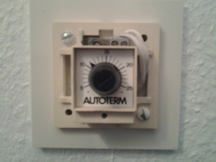 Äldre termostat på vägg, vridknapp, temperaturinställningar, märkt AUTOTERM, beige, använd, enkel installation.