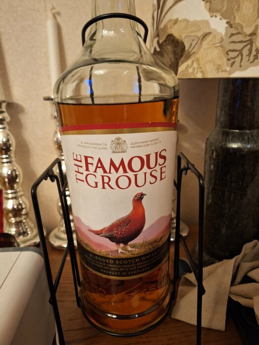 Stor whiskyflaska i ställ, Famous Grouse-etikett, ljus bakgrund, interiördekorationer.