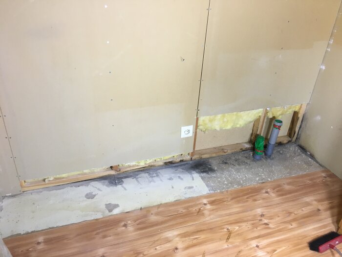 Renoveringsarbete, vägg med gipsskivor, isolering synlig, rörgenomföring, golvet delvis trä, byggstädning behövs.