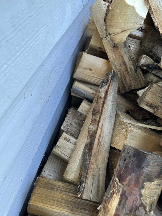 Staplad ved vid en ljusgrå vägg, olika längder och tjocklekar, utomhus belysning.