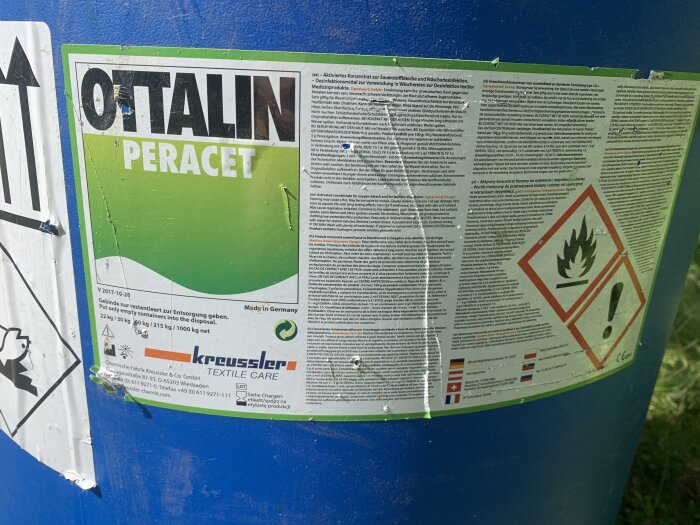 Etikett för kemisk produkt på blå bakgrund, text, varningssymboler, delvis bortslitet, information, klistermärken.