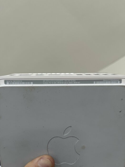 En dator med en äppellogotyp, smutsig yta, serienummer, och en person som håller i den.