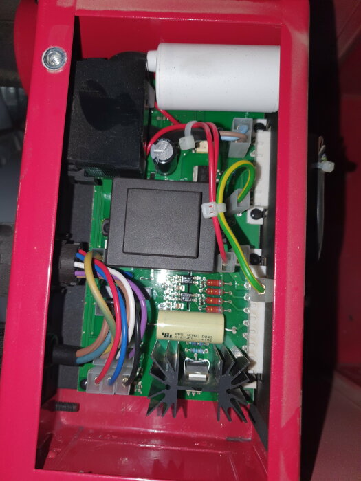 Internt av elektronisk enhet med kretskort, komponenter och kablage i rött skal.