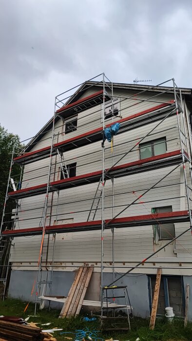 Byggnad med ställningar, renovering pågår, mulet väder, skräp och byggmaterial på marken.