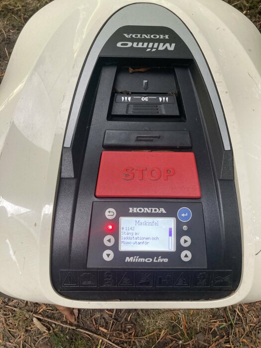 Honda robotgräsklippare kontrollpanel, visar stoppknapp och felmeddelande på skärm, smutsig, utomhusmiljö.