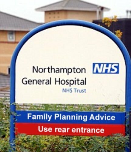 Skylt utanför sjukhus: "Northampton General Hospital", NHS Trust, råd om familjeplanering, använd baksida entré.