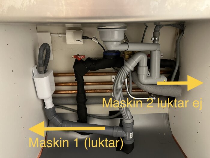 Dubbla avloppssystem under diskbänk, en maskin luktar, den andra gör inte det.