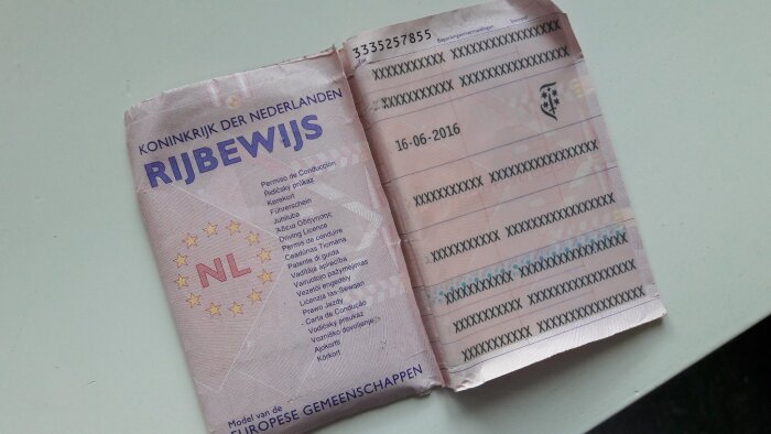 Nederländskt körkort, slitna kanter, information censurerad, EU-symboler, pinkomposition, liggande på bord.