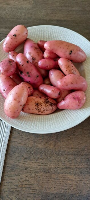 Ett fat med rosa potatisar på ett träbord, några potatisar har jord kvar.