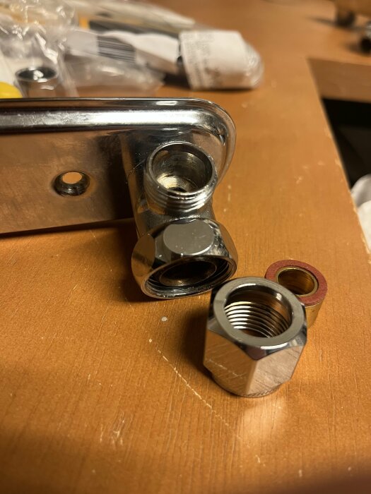 Metalliska föremål, möjligtvis rörkopplingar eller beslag, på ett brunt bord. Bakgrund med suddiga byggmaterial.