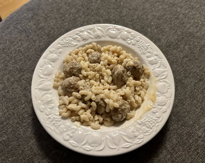 Ett fat med stuvade makaroner och köttbullar, klassisk husmanskost, serverat på ett vitt dekorerat porslinstallrik.