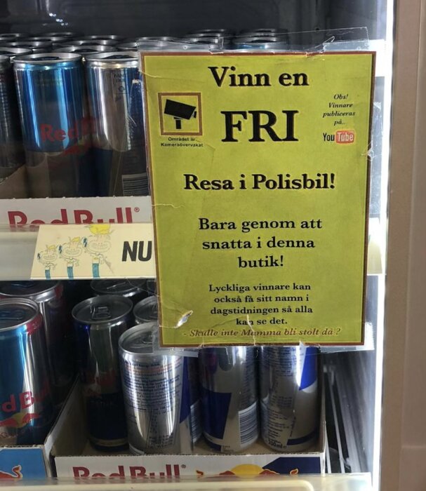 En gul skylt med text erbjuder en "fri resa i polisbil" som ironi för butikstjuvar, omgiven av Red Bull-burkar.