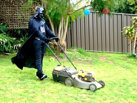 Person klädd som Darth Vader klipper gräset i en trädgård.