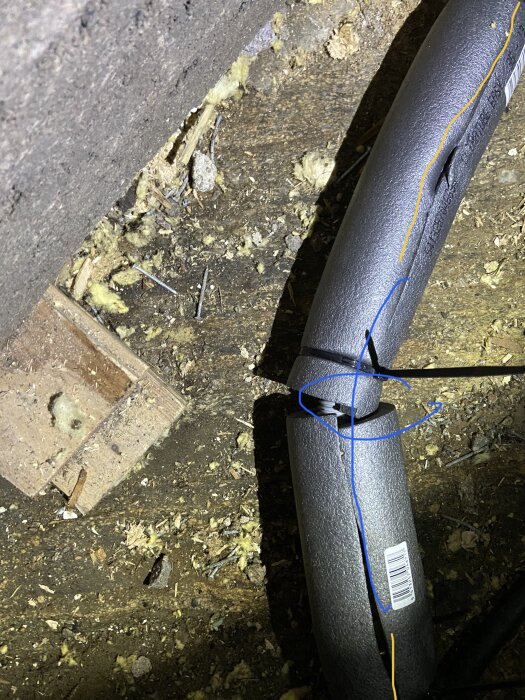 Isoleringsmaterial, trä, spikar, och en kabel på ett stökigt vindsutrymme i dålig belysning.