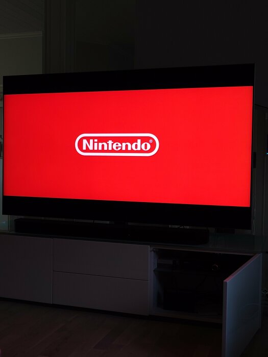 TV-skärm med röd bakgrund och Nintendo-logotyp, i vardagsrum, minimalistisk inredning.