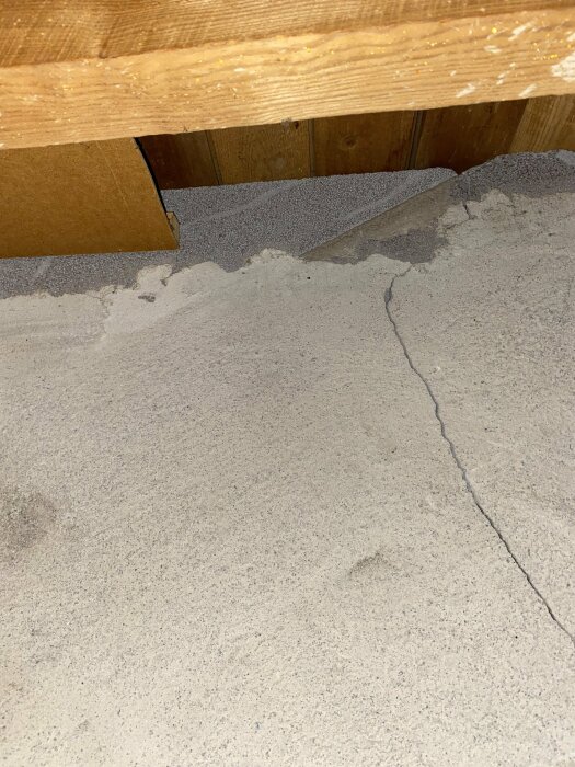 Bild på byggisolering i vindsutrymme, trätakbjälkar, spricka i betong eller puts.