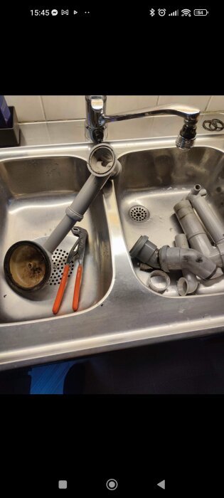 Rostfri diskho med demonterade vattenledningsdelar och en tång. Reparation eller underhåll verkar pågå.