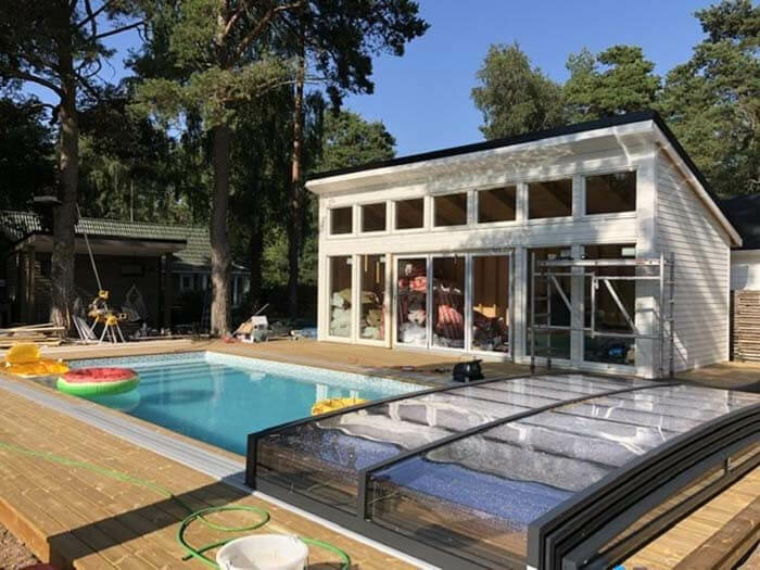 Trädgård med pool, träaltan, moderna hus, soligt, badleksaker, stängd poolöverdrag, avslappnad atmosfär, gröna träd.