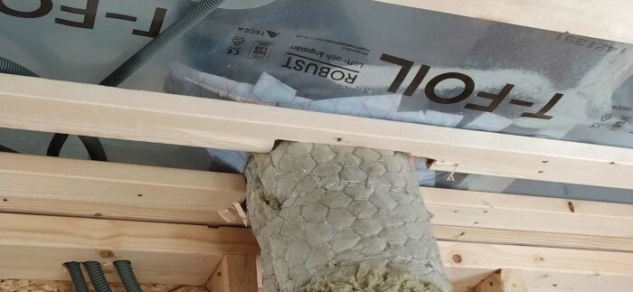 Träkonstruktion och isoleringsmaterial under arbete, byggmaterial synliga, täckplast, ogjord tak eller vägg.