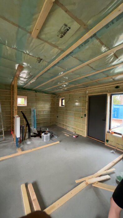 Under konstruktion, isolering i tak, trästommarväggar, fönster, dörr, byggmaterial på betonggolv, inomhus.