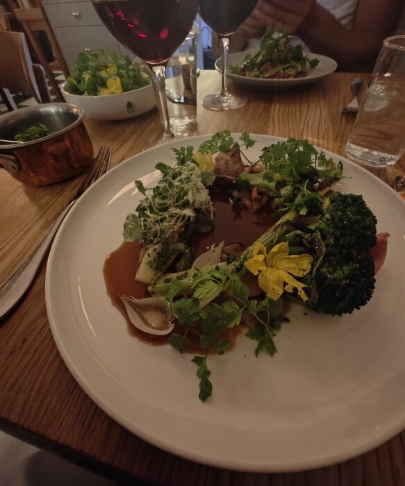 En måltid på restaurang med grönsakstallrik, rödvin, salladskål och person ätandes i bakgrunden.