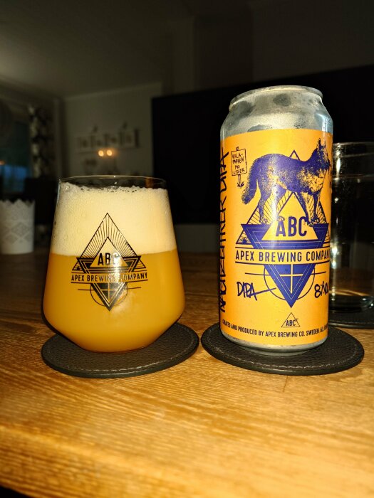 Ett glas öl och ölburk från Apex Brewing Company på ett bord, inomhusmiljö.