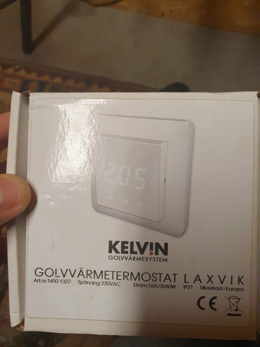 Förpackning av KELVIN golvvärmetermostat LAXVIK, handhållen, teknisk information och CE-märkning synlig.