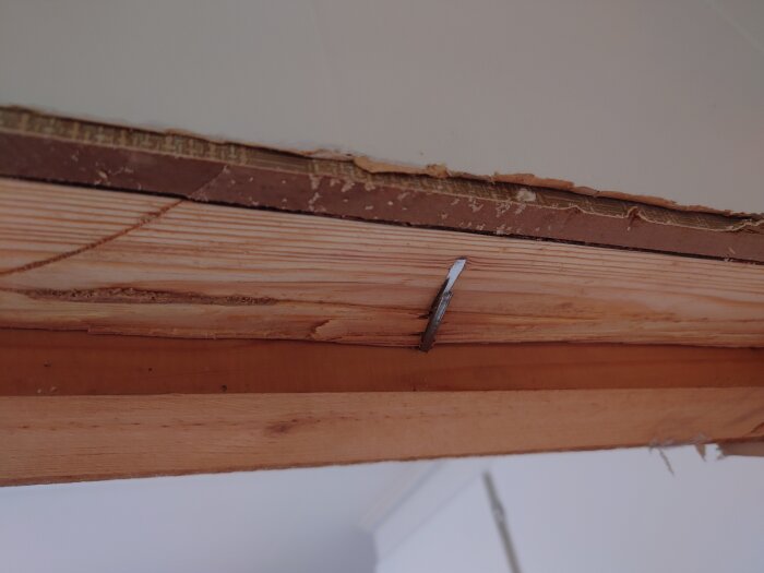 Träbjälkar med en utstickande spik, konstruktion nära tak, ofärdigt byggprojekt eller renovering.